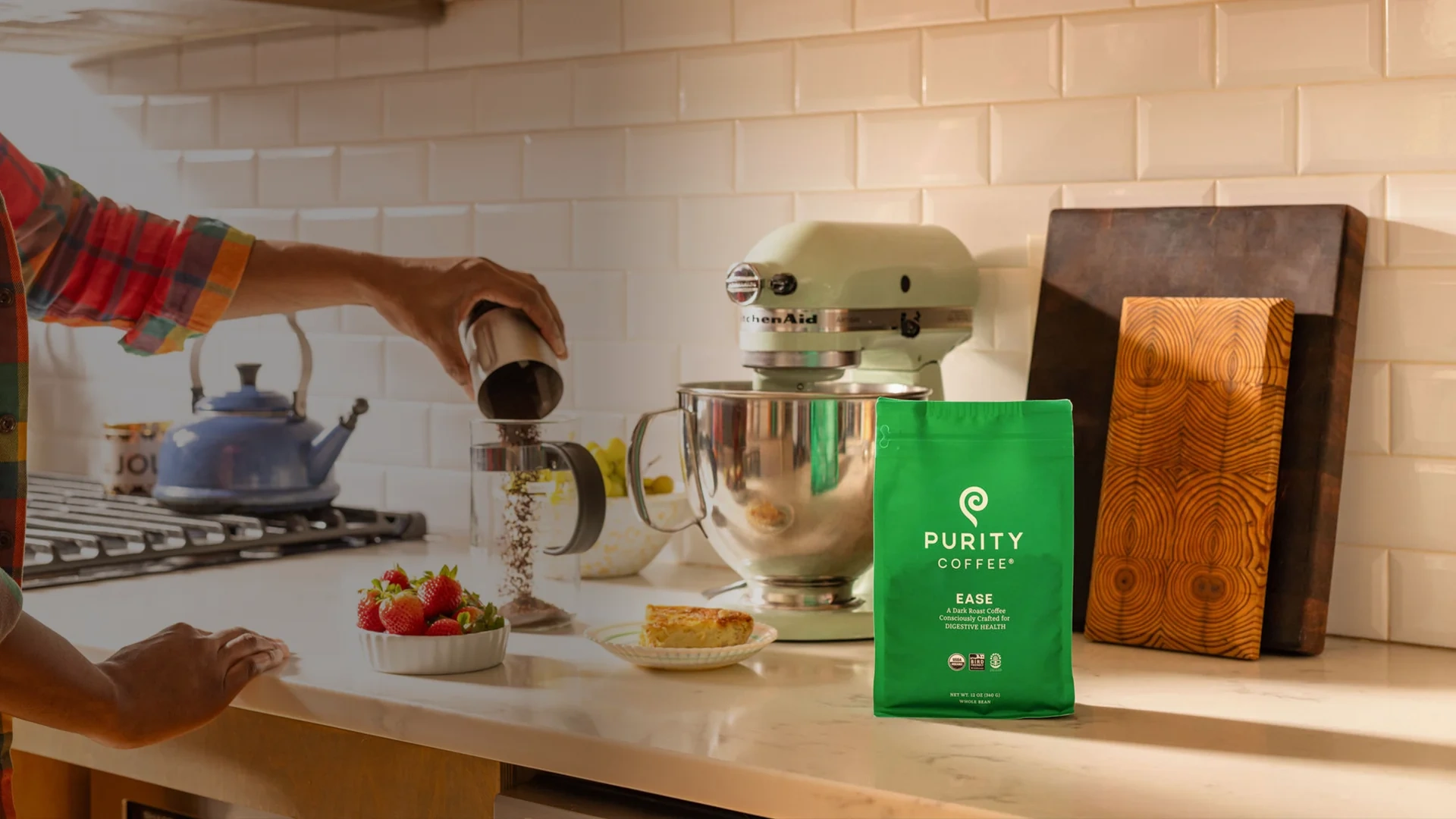 Hands pouring coffee in a bright kitchen beside a green Purity Coffee bag